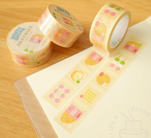 Three rolls of decorative tape with pastel designs on a wooden surface.