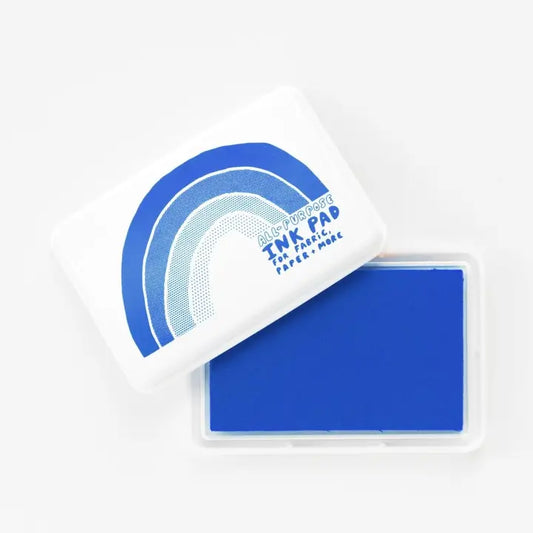 Blue Distressed Ink Pad by Paper + Magic, featuring a white plastic case with a blue and white rainbow graphic, shown with the lid off to reveal a solid blue ink pad inside.