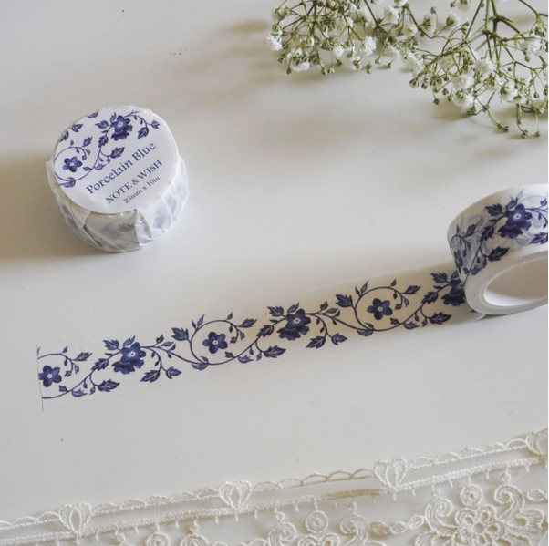 Roll of decorative tape with floral design on a white surface with lace and flowers.