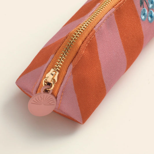 Pencil case with pink and orange striped pattern and gold zipper on a light beige background
