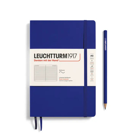 A Leuchtturm1917 A5 softcover notebook in royal blue with a white paper label, shown next to a matching blue pencil on a clean white background.