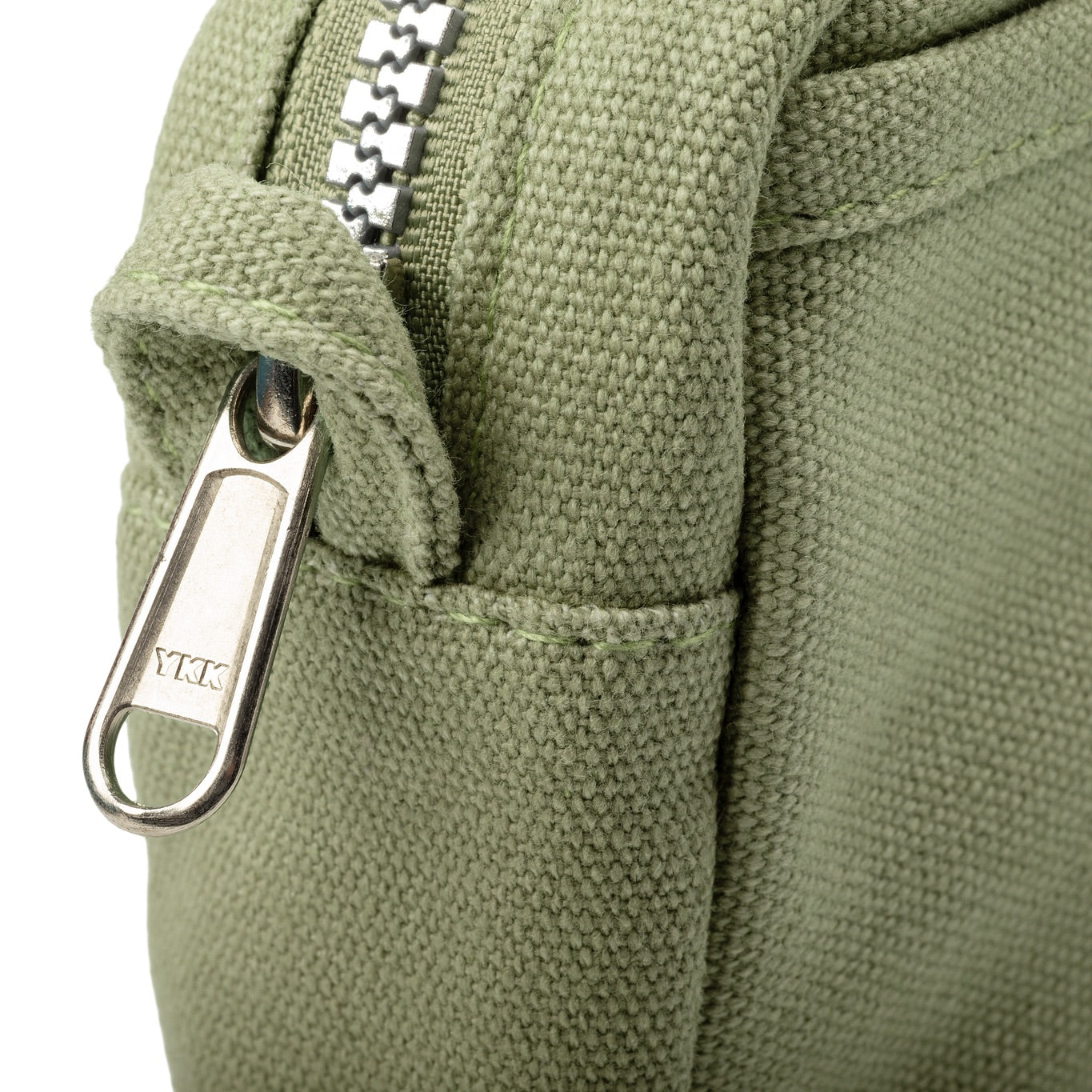 Close-up of a green backpack with a zipper and YKK brand logo.