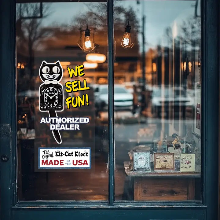 Storefront window with a sign advertising Kit-Cat Klock clocks, reflecting street scene.