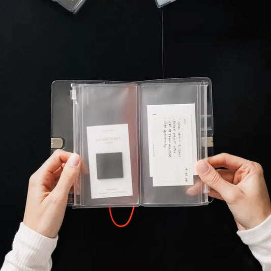 Clear plastic case with printed materials held by hands against a black background