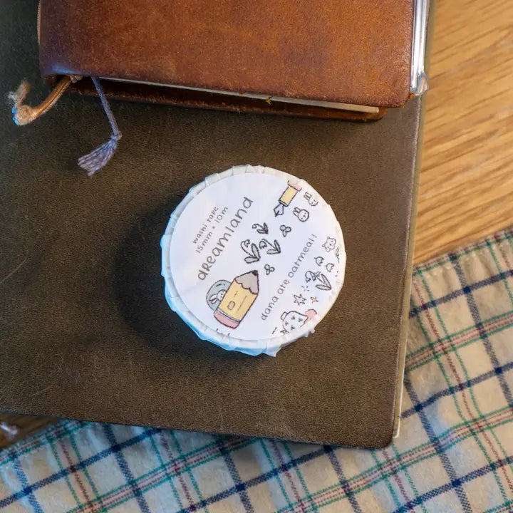 Round container with a label on top of a brown leather-bound book on a checkered fabric surface.