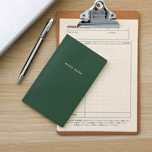 Green memo book on a clipboard with a pen on a wooden surface