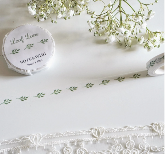 Roll of decorative tape with 'Leaf Lane' branding on a white surface with lace and flowers.