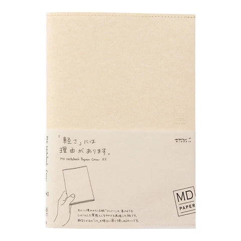 A beige MD Paper notebook with a white paper band around the lower half, featuring Japanese text and a simple line drawing of a hand holding a notebook.