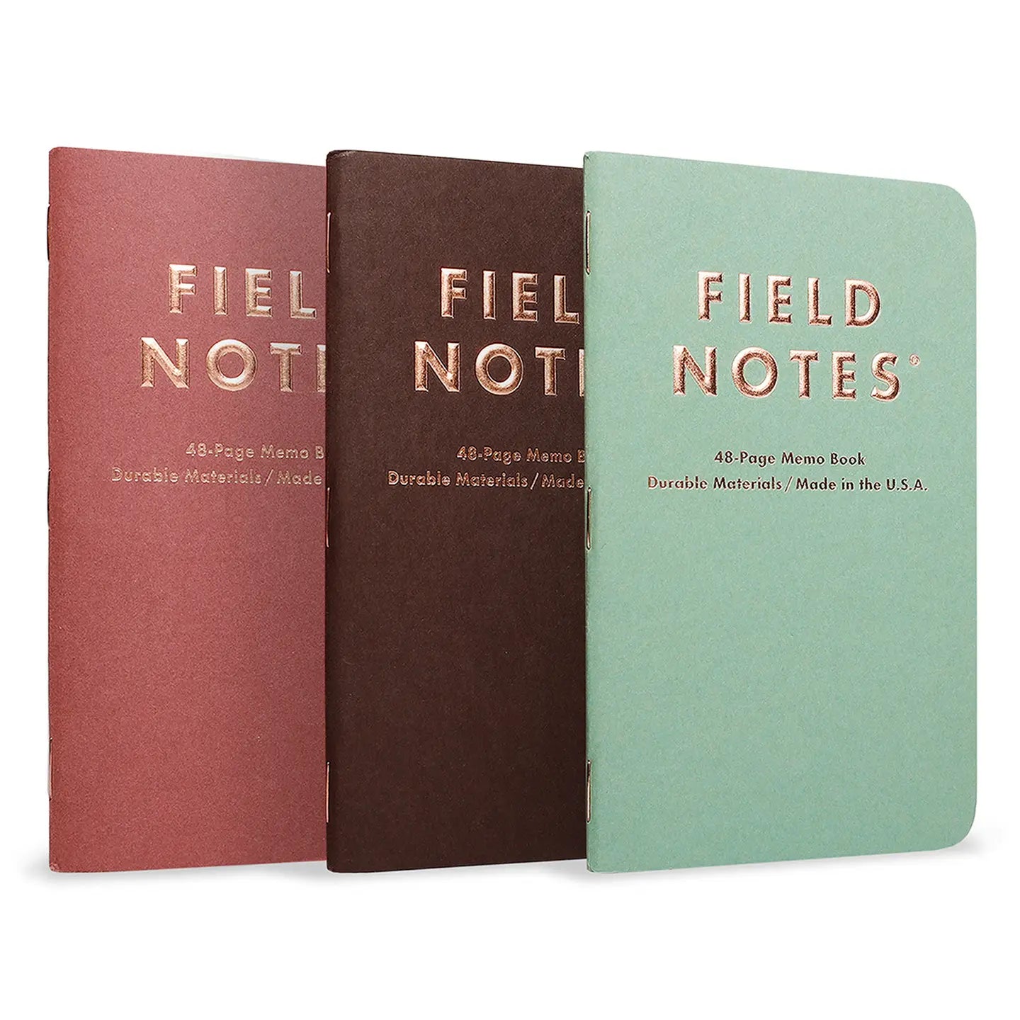 Three 'Field Notes' notebooks in red, brown, and green on a white background