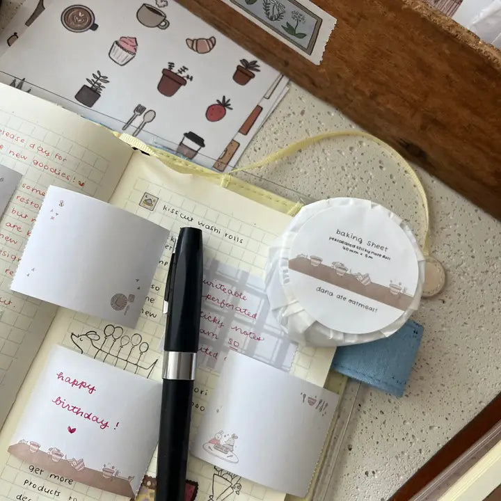 Notebook with stickers, a pen, and a small round object on a textured surface.