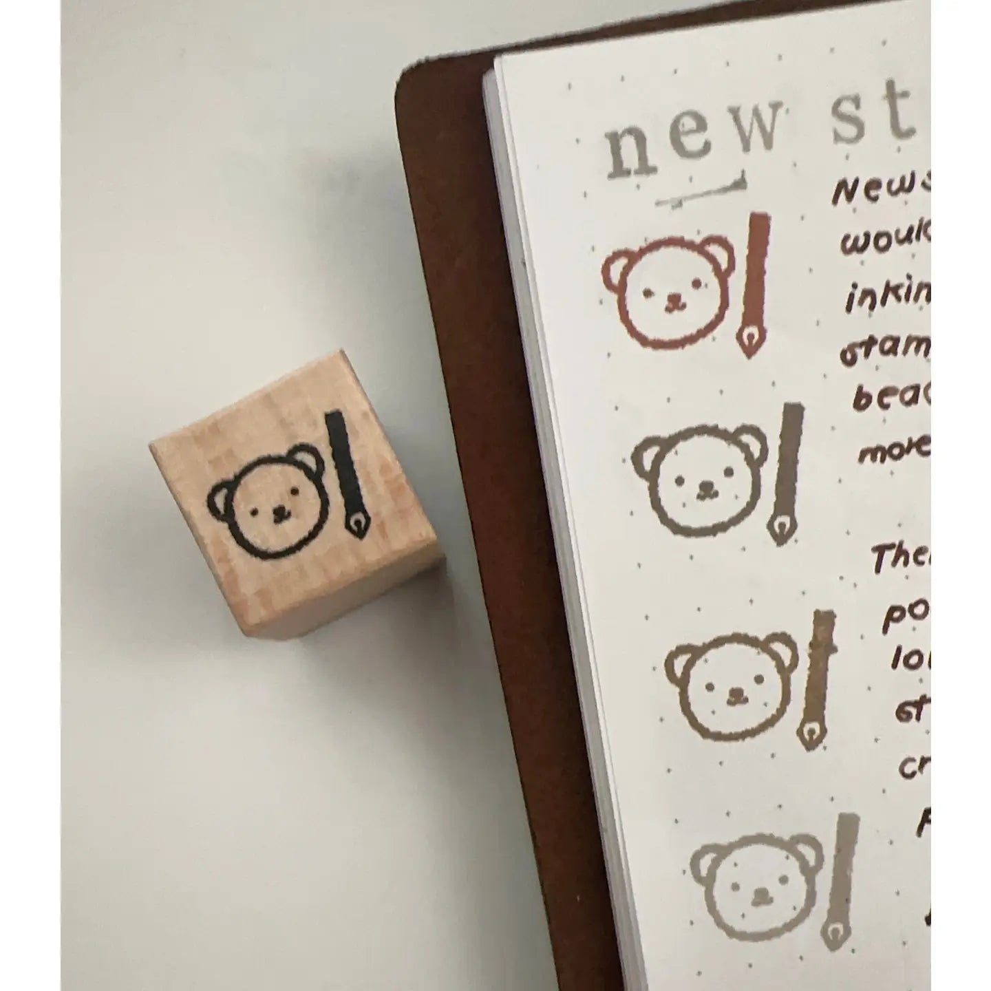 Wooden stamp with bear design next to stamped text on a notebook page.