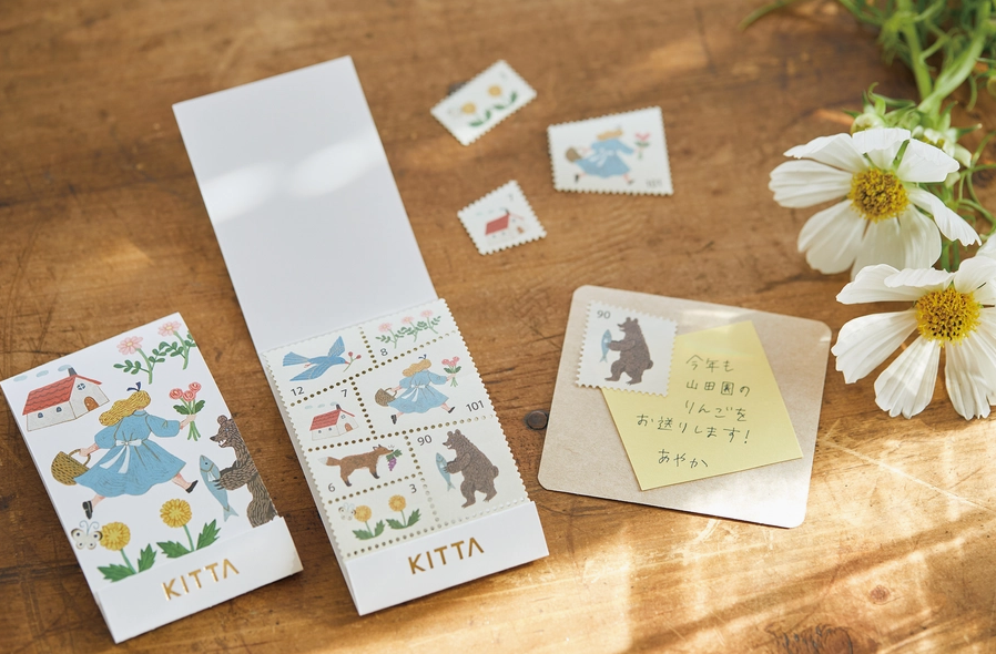 Kittaa stationery set with postcards and stamps on a wooden surface with flowers.