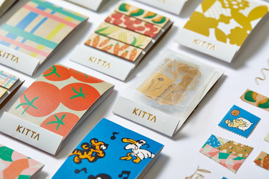Collection of colorful notebooks and postcards with 'Kitta' branding on a white background