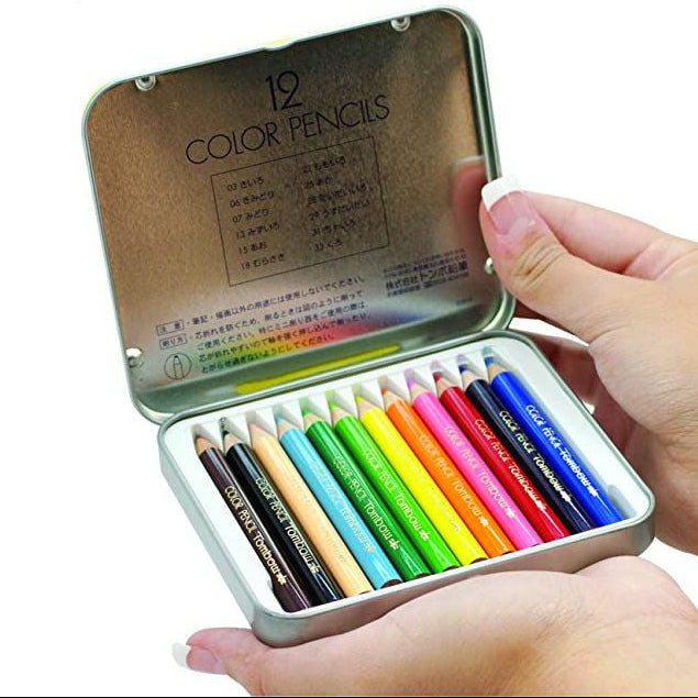 Set of 12 compact size colored pencils in a metal tin held by a hand.