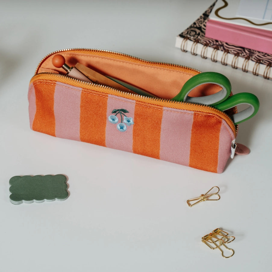 Striped pencil case with green scissors on a light surface