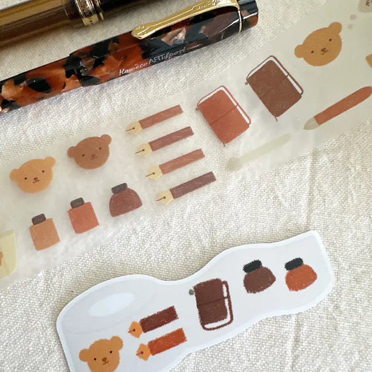 Decorative stickers with bear and book designs on a textured surface with a pen.