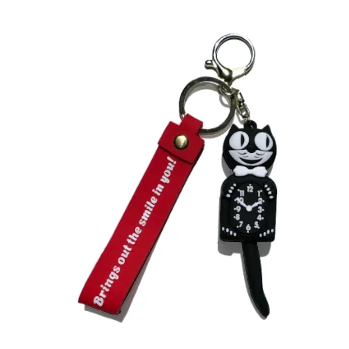 A novelty keychain featuring a black cat-shaped clock with white details and a red strap tag with white text that reads 'Brings out the smile in you!'.
