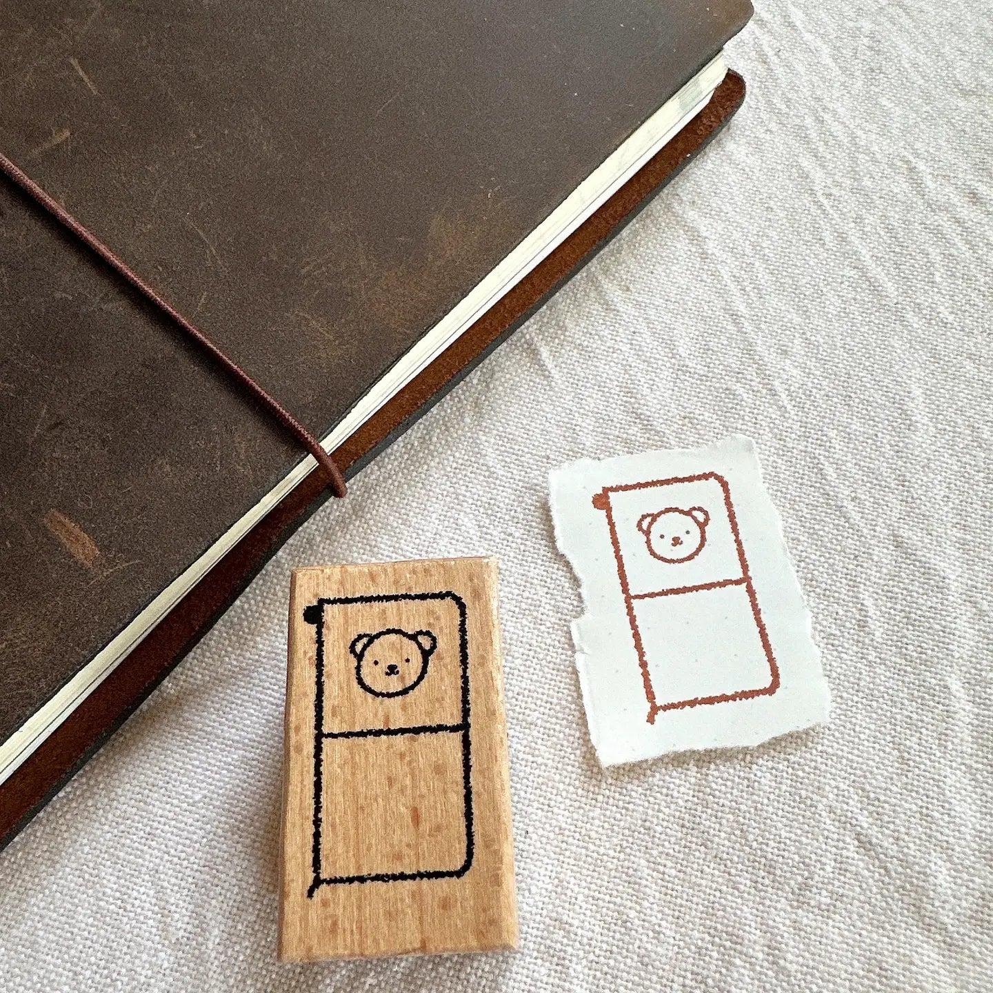 Wooden stamp with bear design next to a printed card on a textured surface