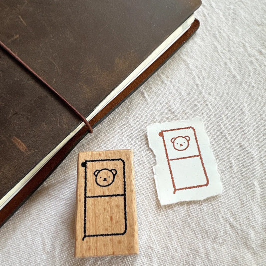 Wooden stamp with bear design next to a printed card on a textured surface