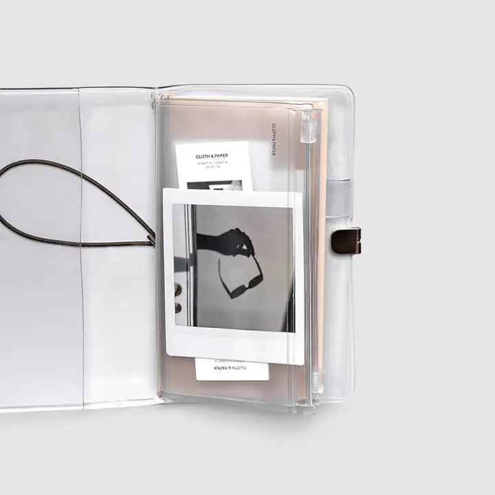A clear acrylic ring binder or file folder shown open on a light gray background, with white paper inserts and a black cord visible inside.