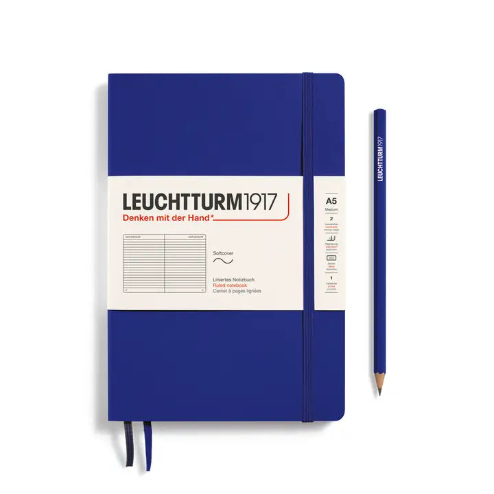 A Leuchtturm1917 A5 softcover notebook in royal blue with a white paper label, shown next to a matching blue pencil on a clean white background.