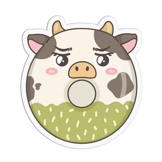 A die-cut cartoon cow face sticker or decal on a plain white background. The cow has a white face with dark brown patches, pink ears and cheeks, a peach snout, and a green lower section with small white speckles.