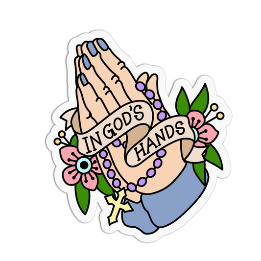 A die-cut sticker featuring a traditional tattoo-style illustration of praying hands with a rosary, pink flowers, green leaves, and a banner reading 'IN GOD'S HANDS'.