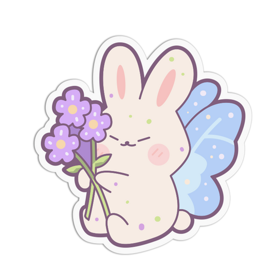 A cute cartoon bunny sticker or decal with pastel colors. The bunny is cream-colored with pink inner ears, closed eyes, a pink blush, green speckles, and light blue wings, holding three small purple flowers with green stems.