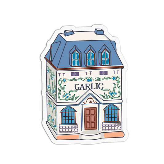 A die-cut sticker featuring a whimsical illustration of a house with blue roof and windows, floral details, and the word 'GARLIC' across the front, shown on a plain white background.