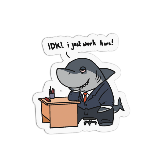 A die-cut cartoon sticker featuring a gray shark dressed in a dark suit and tie sitting at a desk with a speech bubble that reads, 'IDK!, i just work here!' on a plain white background.