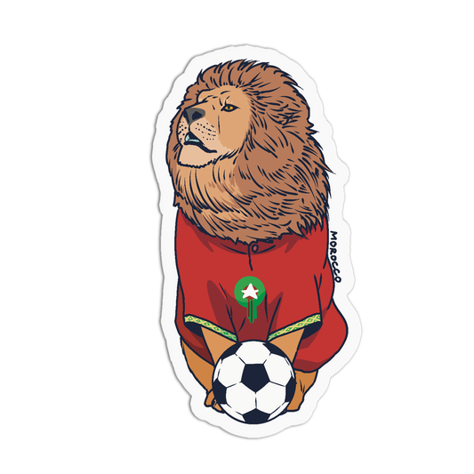 A die-cut sticker featuring an illustrated lion wearing a red Morocco soccer jersey and holding a soccer ball, shown on a plain white background.