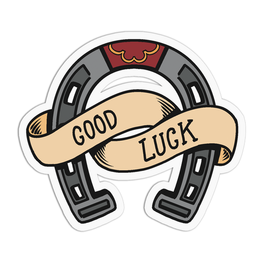 A die-cut sticker featuring a horseshoe with a beige banner across it that reads 'GOOD LUCK' in black text, on a white background.