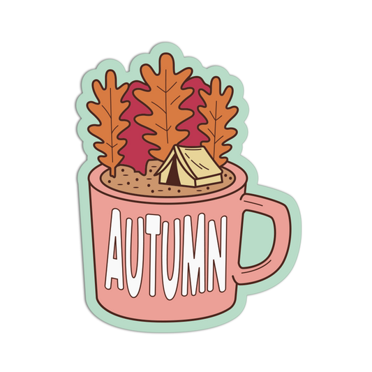A die-cut sticker featuring an autumn-themed illustration of a pink mug with the word 'AUTUMN' in white, filled with brown leaves, a small beige tent, and a light green outline, shown on a plain white background.