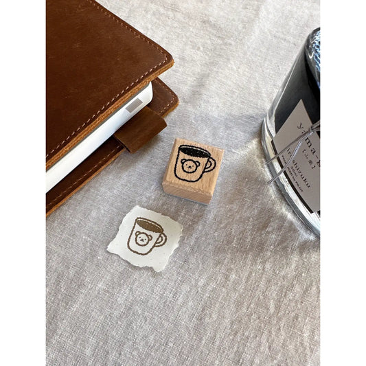 Rubber stamp with a coffee cup design on a textured surface next to a ink pad.