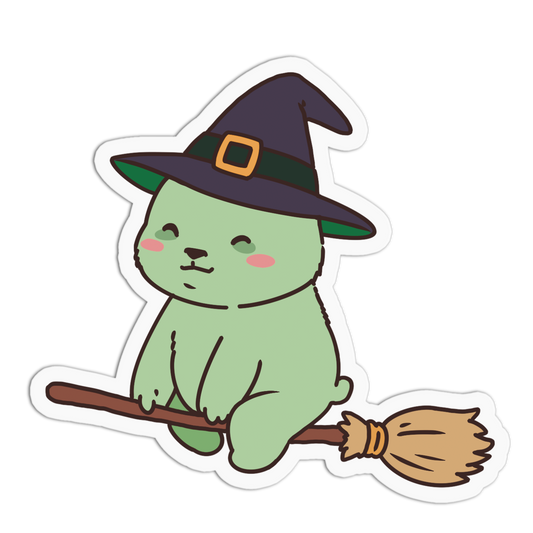 A die-cut sticker featuring a cute light green cartoon bunny wearing a dark purple witch hat with a gold buckle and sitting on a brown broomstick, shown on a plain white background.