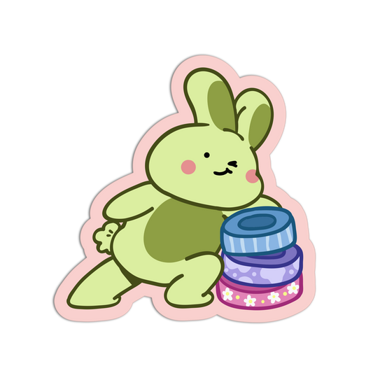 A cartoon bunny sticker or decal in light green with darker green ears and belly, pink cheeks, and a pink outline, shown next to a stack of three patterned jars on a plain white background.