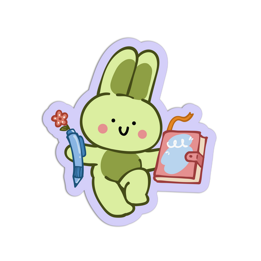 A cartoon bunny sticker or decal on a plain white background. The bunny is light green with darker green inner ears, holding a blue pen with a small red flower and a pink notebook with a blue page.