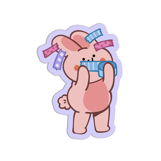 A cartoon bunny sticker or decal on a plain white background. The bunny is light pink with darker brown outlines, wearing a blue striped diaper and several colorful hair clips in pink, purple, and blue.