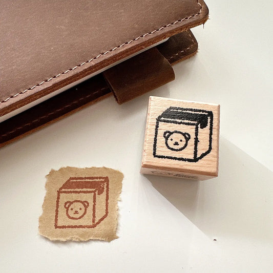Rubber stamp with bear design on a piece of paper next to a brown leather notebook.