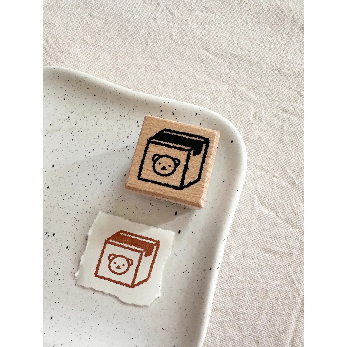 Wooden stamp with a design of a box and bear on a speckled ceramic plate.