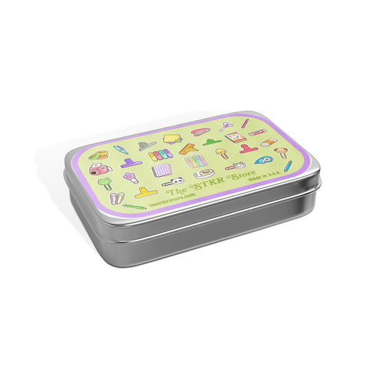 A rectangular silver metal tin with a light green lid featuring colorful illustrated icons and the text 'The STKR Store' and 'SEY 120g'.