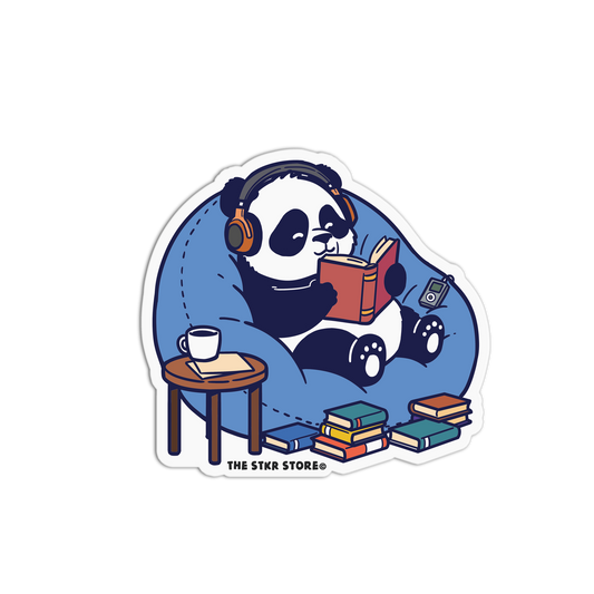 Sticker of a panda reading a book with headphones on, sitting on a bean bag chair with books around, on a white background.