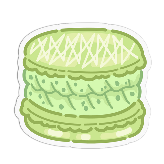 A die-cut sticker featuring a cute, cartoon-style illustration of a light green macaron with white cream details, shown on a solid white background.