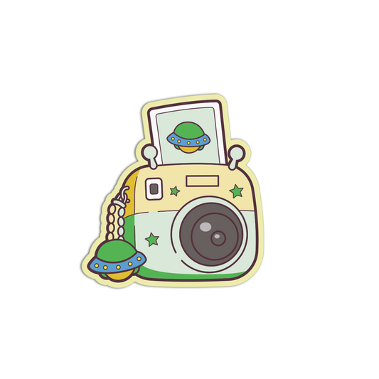 A cartoon-style camera sticker featuring a retro design with green stars, a green UFO, and a matching UFO charm, shown on a plain white background.