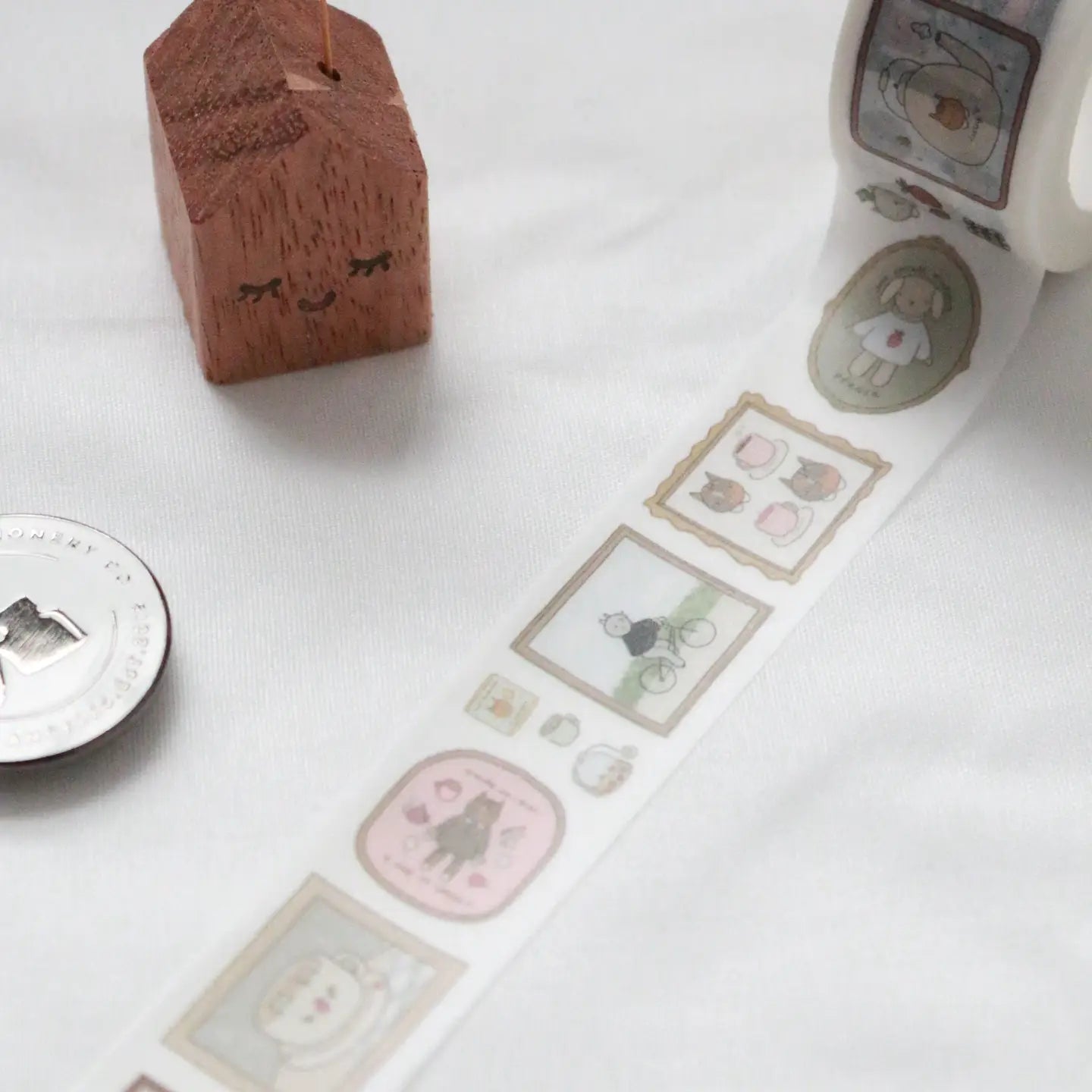 Roll of decorative tape with cute illustrations on a white surface, next to a wooden block and metallic object.