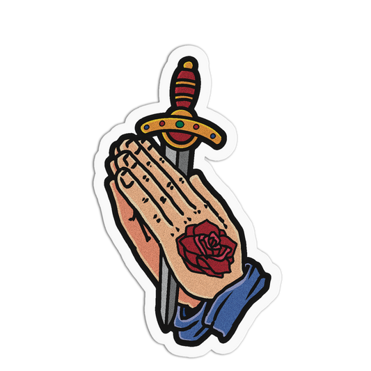 A die-cut sticker featuring a traditional tattoo-style illustration of praying hands holding a sword with a red rose tattoo on the back of one hand, set against a plain white background.